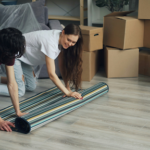 Unmarried couple unpacking boxes and laying a rug in their new home after moving in together