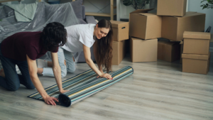Unmarried couple unpacking boxes and laying a rug in their new home after moving in together Unmarried couple unpacking boxes and laying a rug in their new home after moving in together
