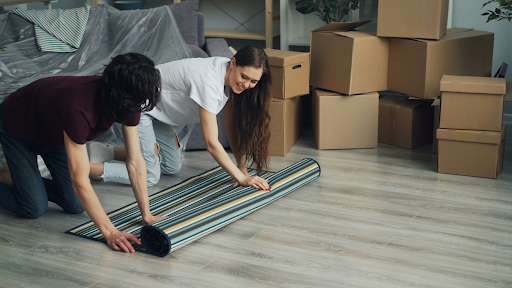 Unmarried couple unpacking boxes and laying a rug in their new home after moving in together